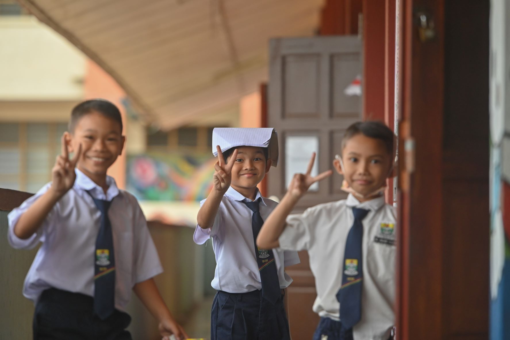 Tiga murid sekolah tersenyum sambil membuat gaya peace sign